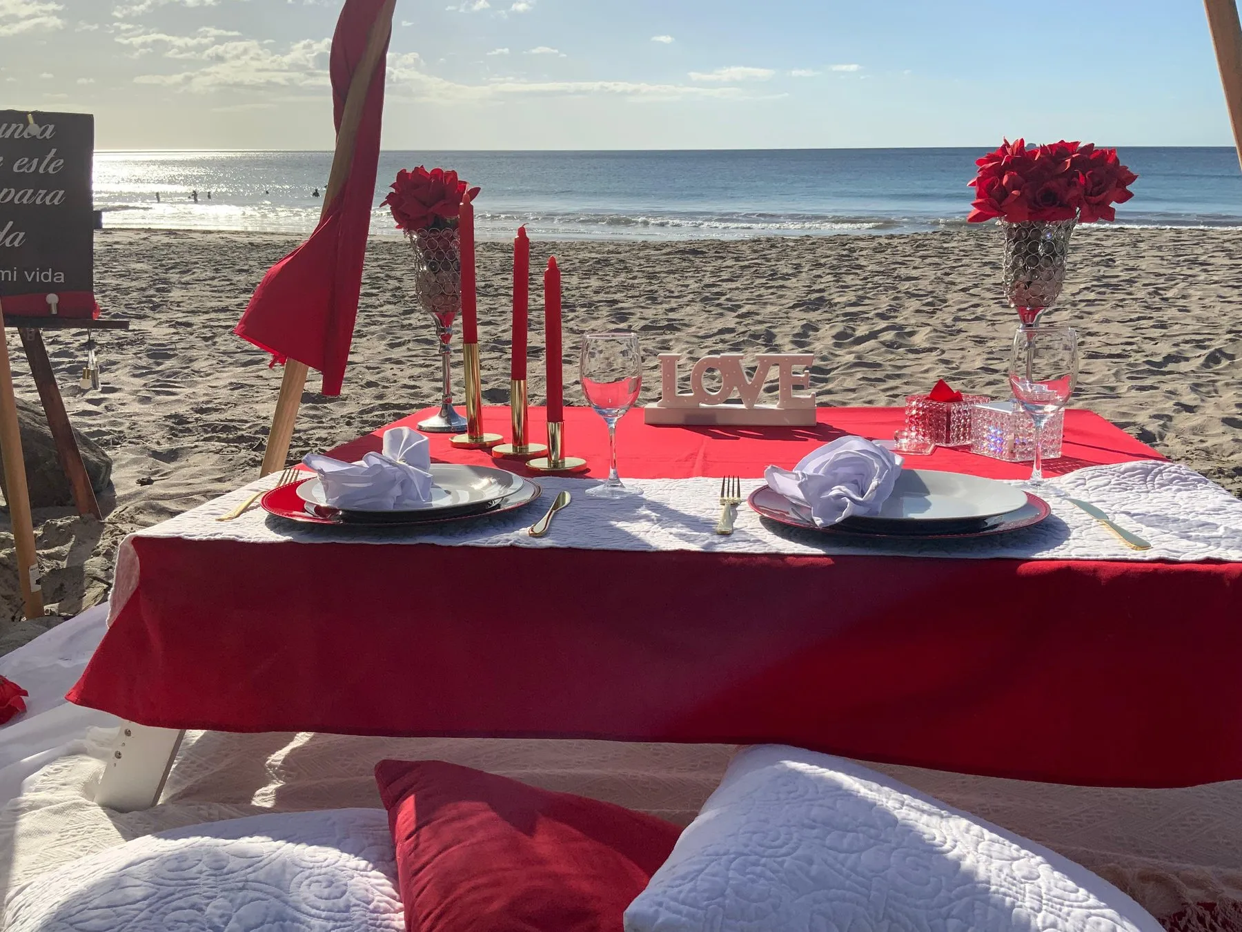 Cena romántica en la playa con mantel rojo, velas y rosas