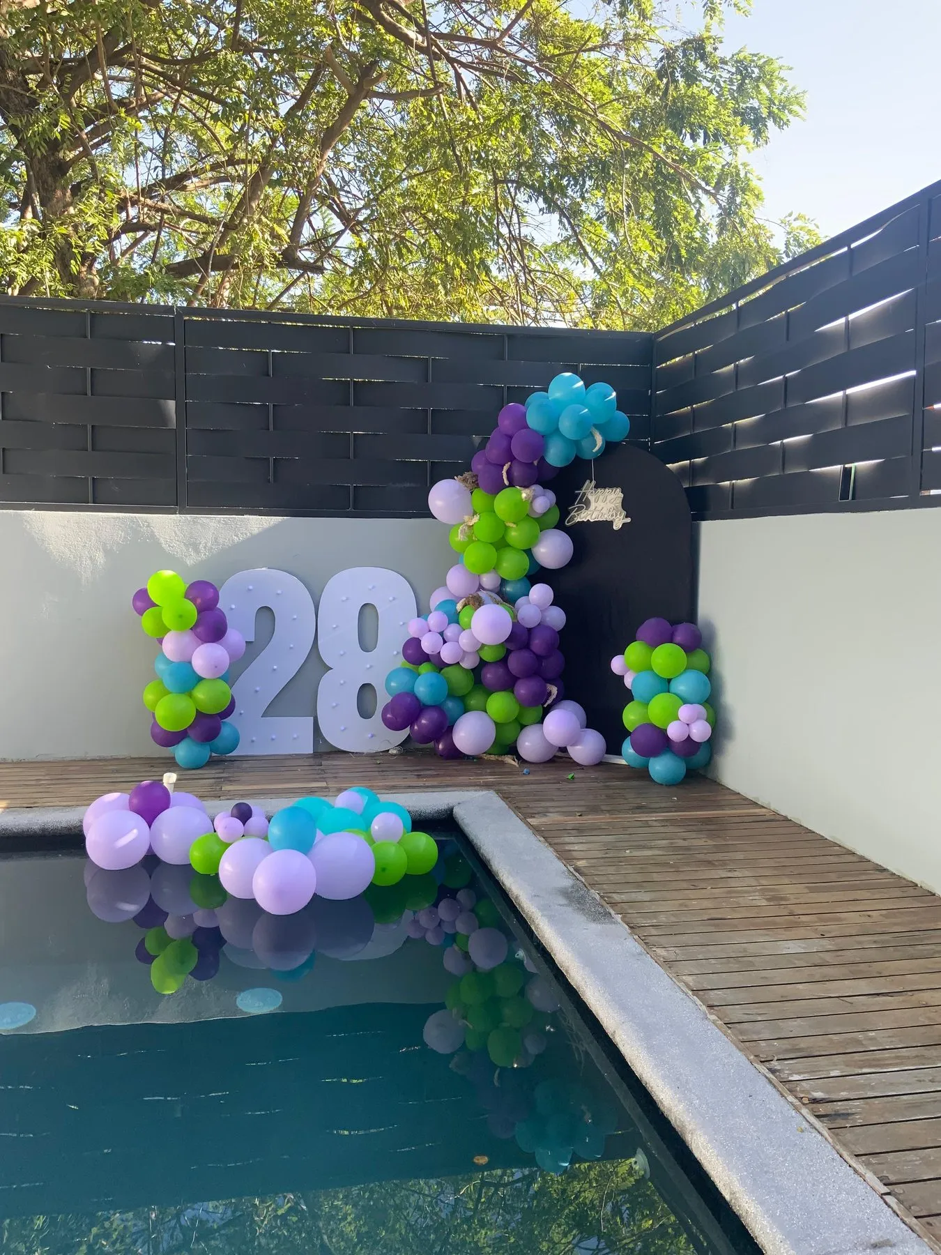 Cumpleaños 28 con globos morados y verdes junto a la piscina