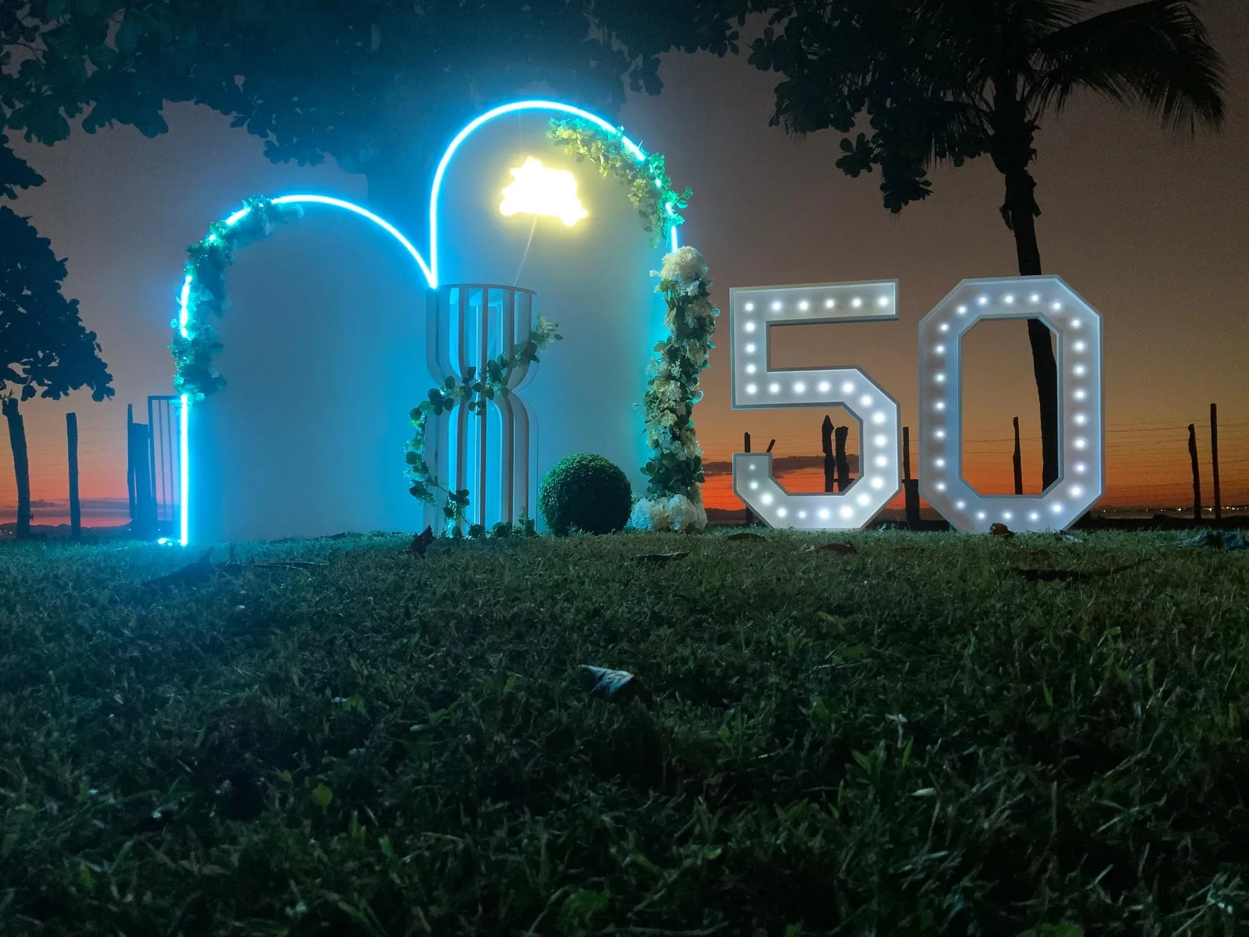 Cumpleaños 50 con arcos iluminados y números gigantes al atardecer