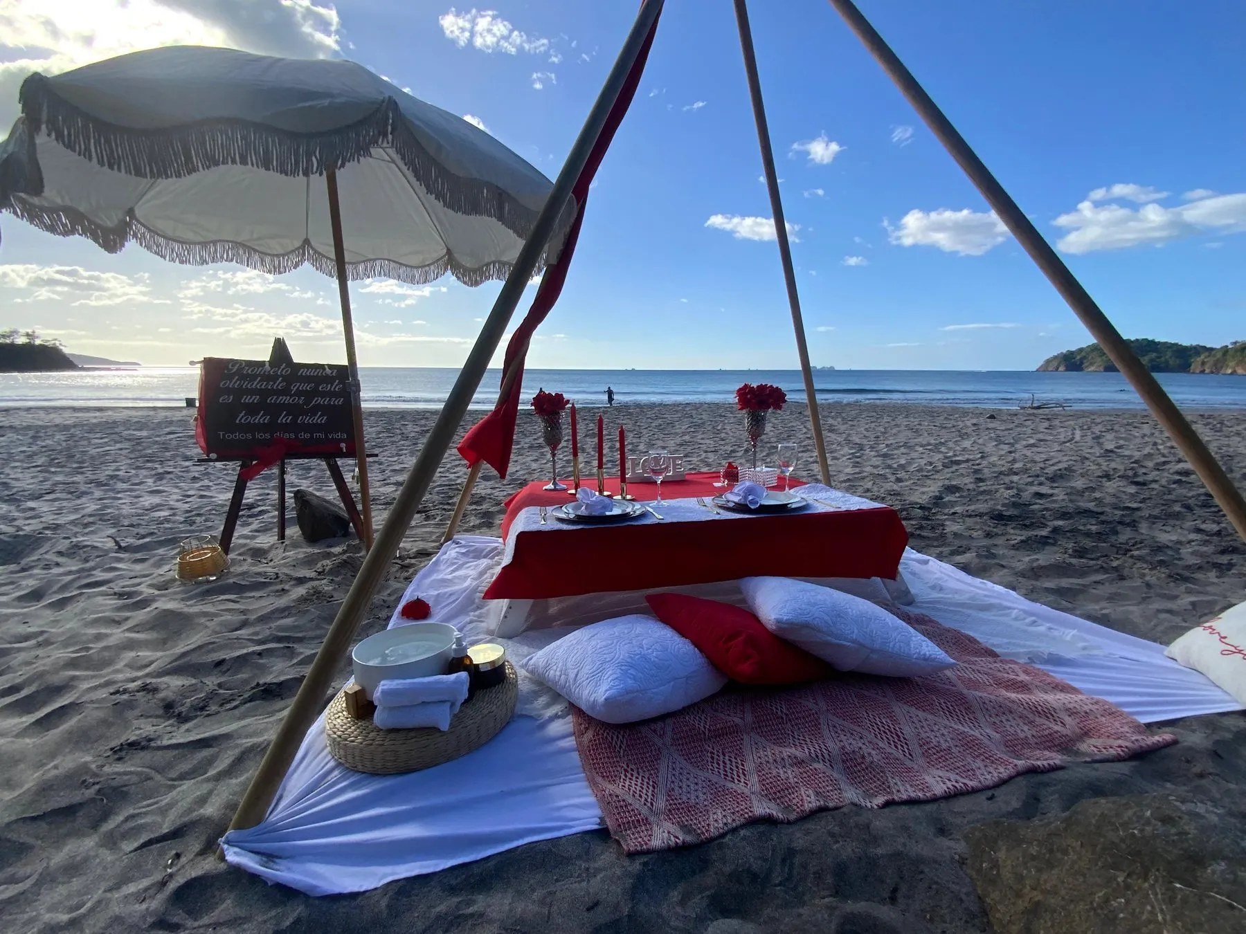 Picnic en la playa con mantel rojo, cojines y sombrilla